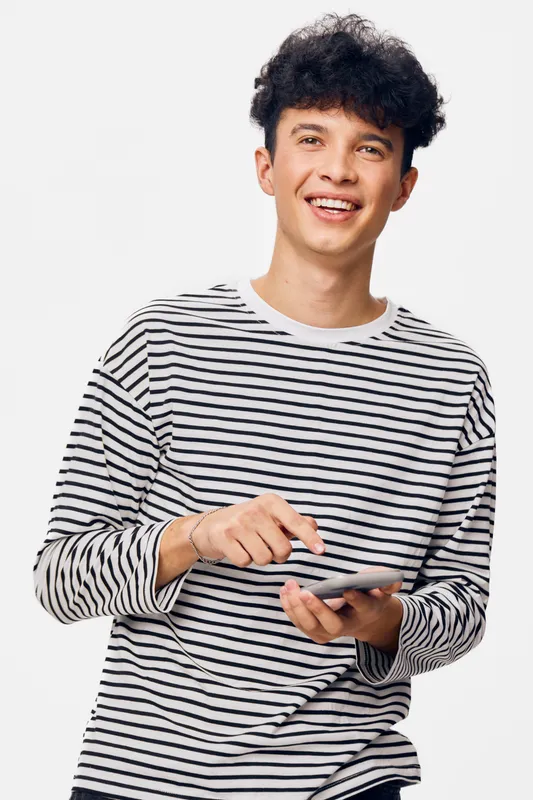 young man smiling and using smartphone with striped shirt against white background, cheerful expression and casual modern style, technology and communication