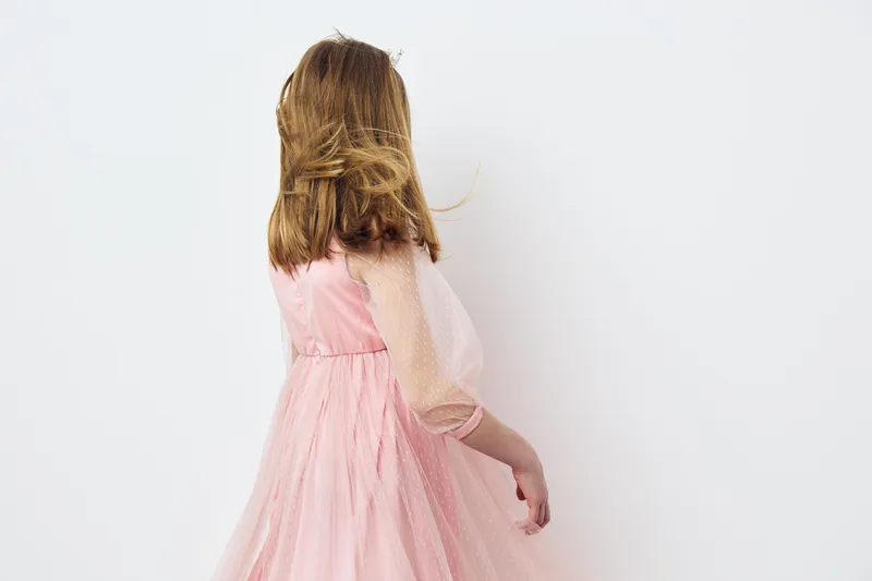 A young girl in a pink tulle dress with flowing hair, expressing joy while facing away against a clean white background, ideal for children s fashion and happiness concepts