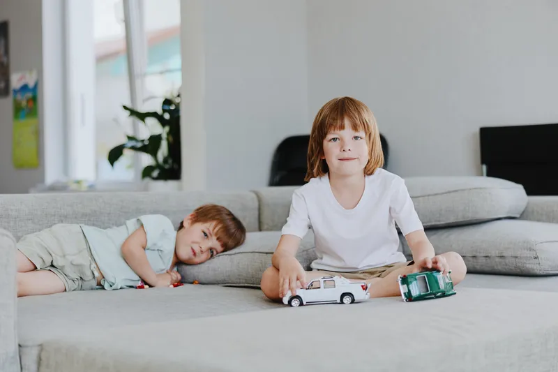 Two playful boys enjoying their time indoors, playing with toy cars on a cozy sofa. Their laughter fills the room with joy and warmth.