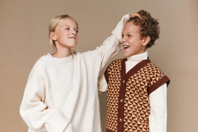 Authentic scene of playful friends sharing a light moment, showcasing cozy fashion and sincere interaction in a casual school lifestyle setting, with warm tones and relaxed mood.