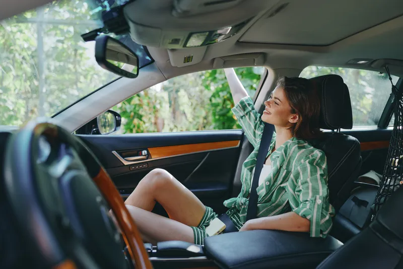 A woman sits in the car seat, relaxed and ready for a drive, with a subtle smile and comfortable posture.