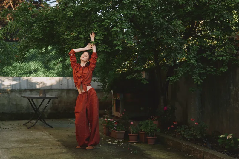 Woman in red dress dances gracefully in a garden outdoors capturing a lifestyle moment of movement and calm contentment bright greenery surrounds her inviting creative relaxation