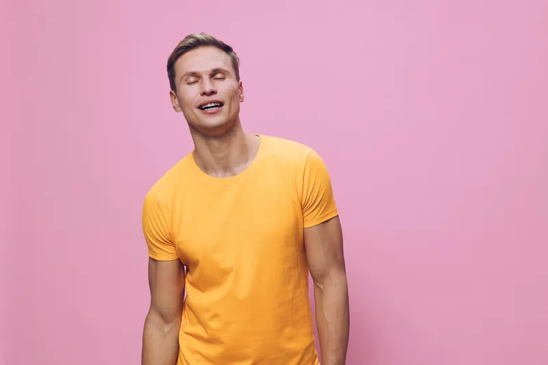 Smiling young man in yellow t-shirt with short hair and fair skin posing against pink background, looking cheerful and relaxed, studio portrait, casual style, happy emotions, lifestyle concept