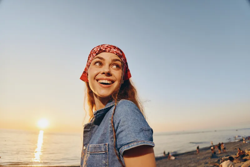 lifestyle woman with modern boho-western denim street style smiling outdoors during golden hour with warm film color tones and a serene beach background