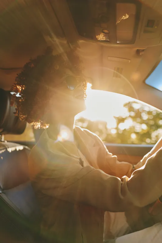 driver woman in a car with steering sunlight through the window at sunset, reflections on the interior, candid travel mood, retro vibe and golden hour glow