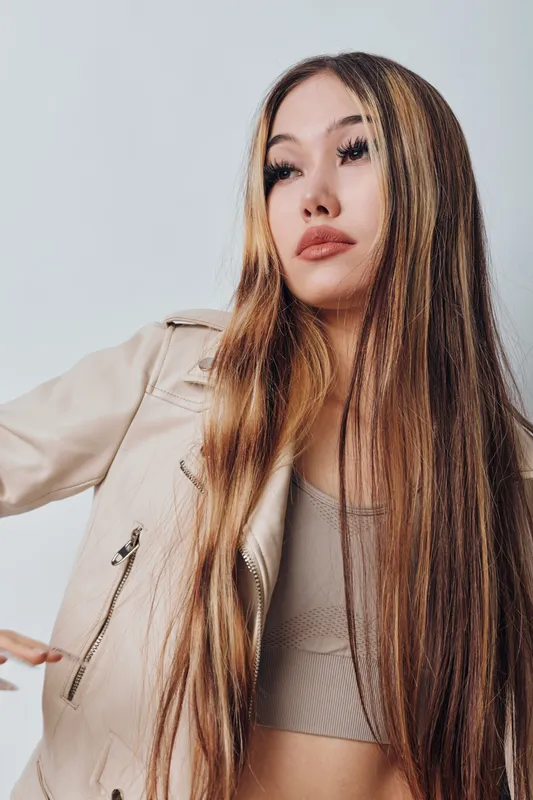 Young woman with long straight hair wearing beige jacket and crop top posing isolated on light background with confident expression and relaxed posture in studio portrait.