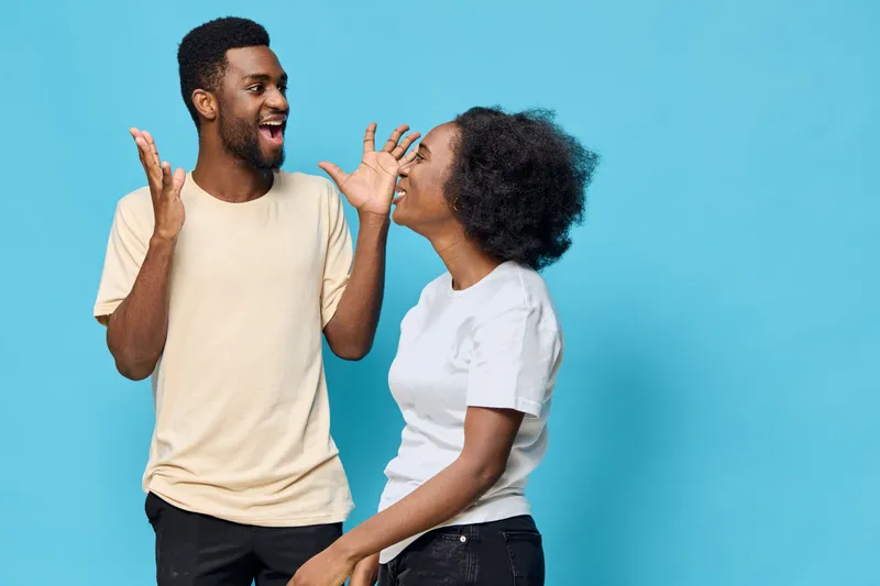 Joyful young African American couple celebrating with excited expressions against a bright blue background, showcasing happiness and connection in casual outfits