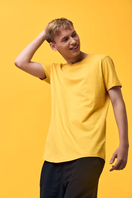 Young man wearing a yellow t shirt poses casually against a bright yellow backdrop, showcasing relaxed fashion and a cheerful everyday vibe, with vivid color harmony for lifestyle branding