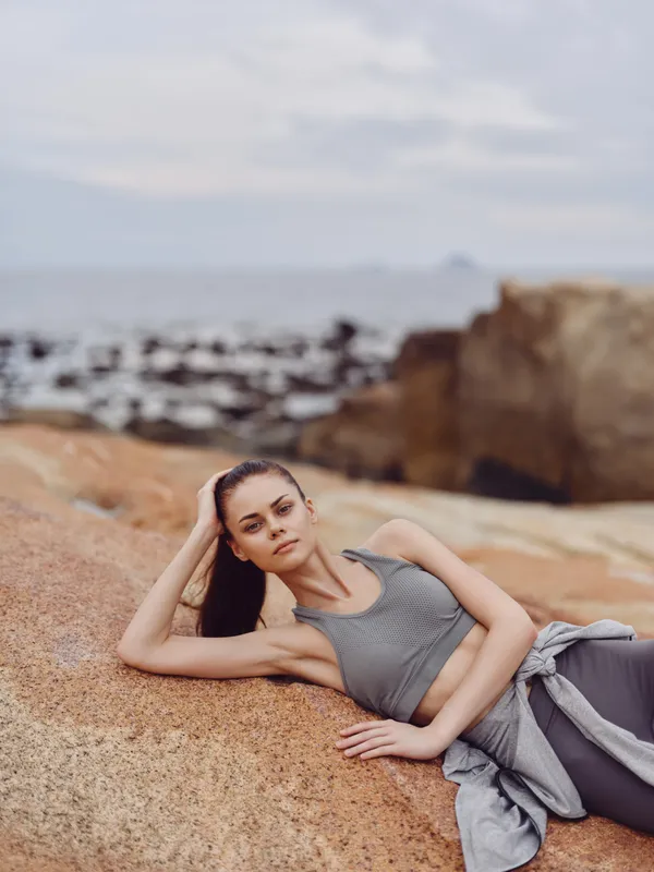 Young woman in athletic wear relaxing on rocky beach, showcasing tranquility and active lifestyle in a natural setting