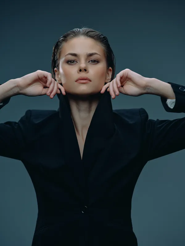 Confident woman in black jacket with wet hair, posing against a dark blue background, showing strength and elegance.