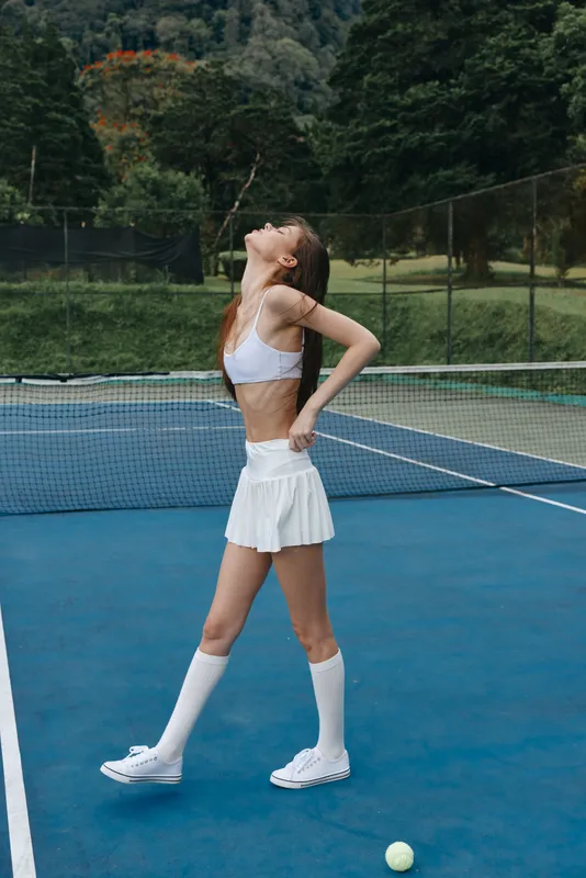 Young female tennis player, looking confident and joyful, in a sporty white outfit on a vibrant blue court, ready for a match with a tennis ball