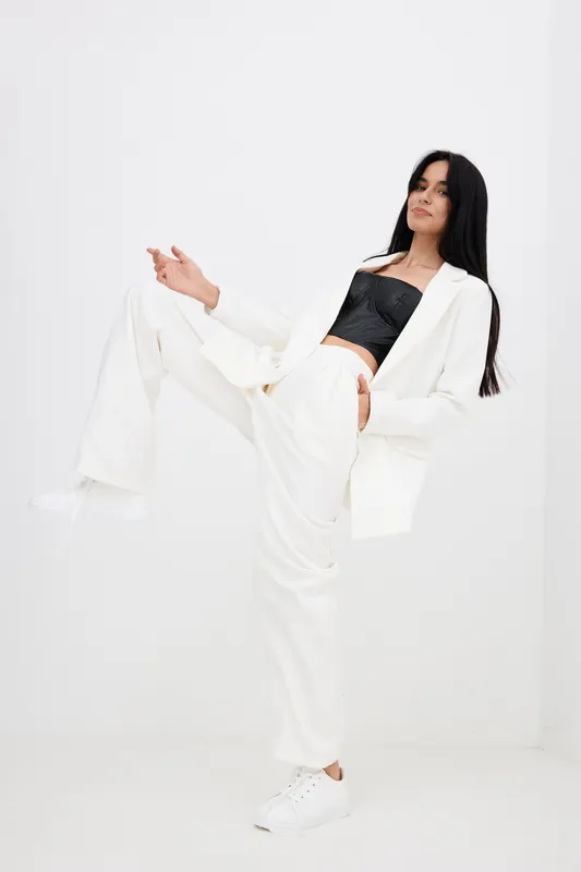 stylish woman posing confidently in white suit and black top, showcasing modern fashion, casual elegance, and dynamic movement on plain white background