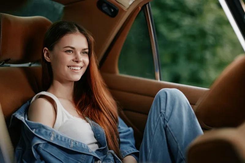 Young woman with long hair in casual outfit smiling in a car, embodying joy and freedom in an outdoor setting, perfect for lifestyle concepts.
