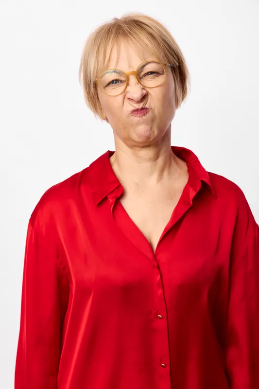 Woman with glasses in a red shirt, senior portrait against a white studio background. Neutral expression, calm mood, soft even lighting, headshot closeup.