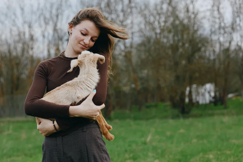 Cheerful woman outdoors, gentle embrace with a young goat kid, sunlit meadow, soft breeze, relaxed mood, natural colors, candid lifestyle moment, rural charm