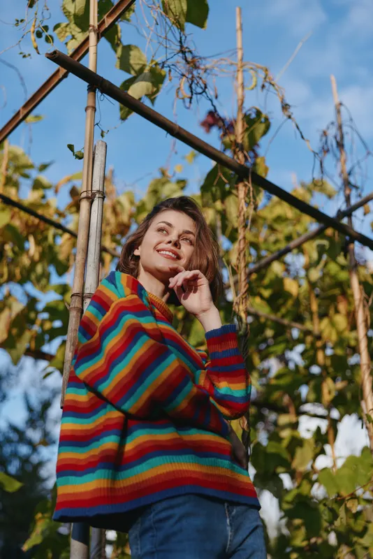 woman portrait in colorful sweater smiling outdoors in a garden setting, casual autumn fashion, standing by trellis with leaves, natural light and relaxed expression