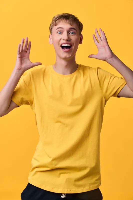 Brightly lit, excited young man in a yellow shirt shows energy and surprise, capturing playful emotion and motion for upbeat lifestyle and fashion concepts scene