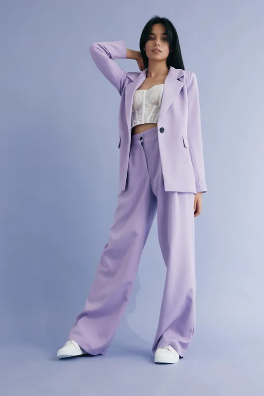 stylish woman in lilac suit standing confidently against a soft purple background wearing a lace crop top and white sneakers, modern fashion outfit