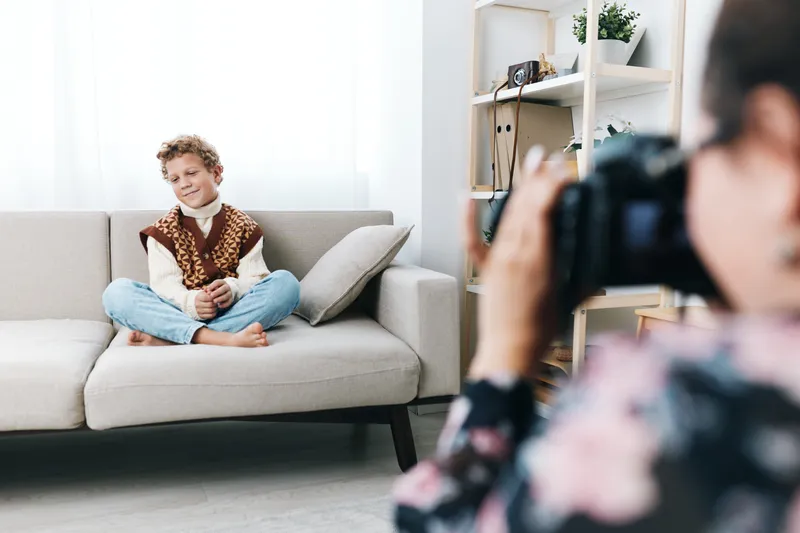Authentic candid portrait of a young student seated on a sofa at home while a photographer captures a spontaneous moment, highlighting everyday school life and genuine emotion.