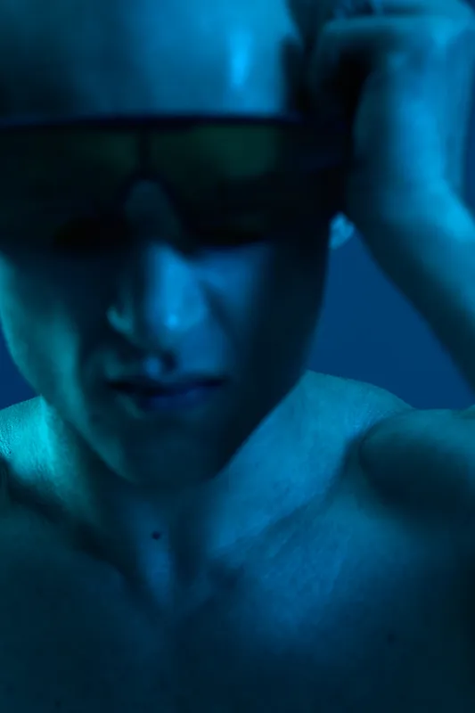 Young man in stylish sunglasses, showcasing a confident expression with a blue hue. The image captures a modern, vibrant feel in a striking light setting.