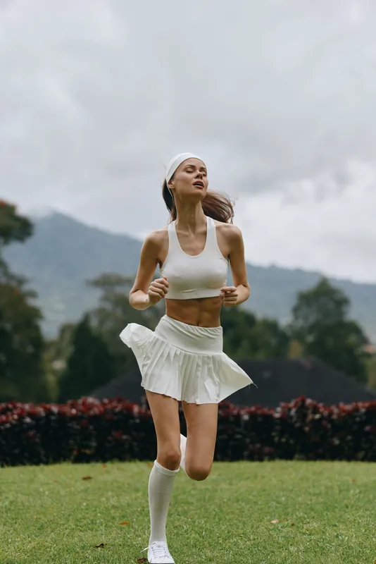 Young athletic woman jogging in a scenic outdoor park wearing a white sports outfit, expressing joy and energy, ideal for healthy lifestyle concepts