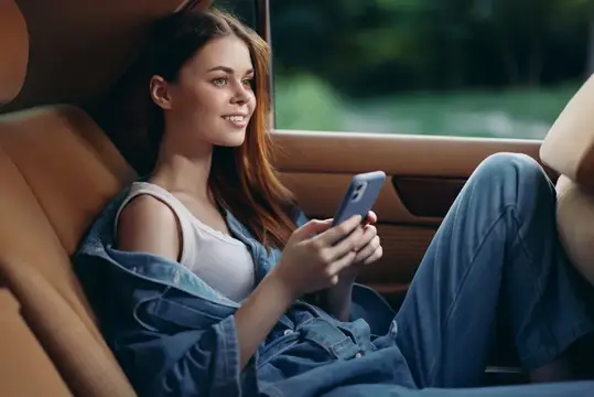 Улыбающаяся девушка со смартфоном сидит в салоне автомобиля