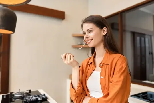 Улыбающаяся девушка пробует еду с ложки на кухне
