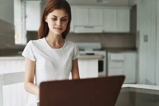 Рыжеволосая женщина работает за ноутбуком на светлой кухне