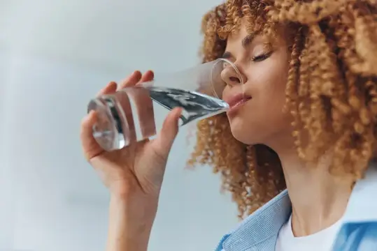 Кудрявая девушка пьёт воду из стеклянной бутылки