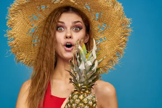 Удивлённая девушка в соломенной шляпе с ананасом на синем фоне