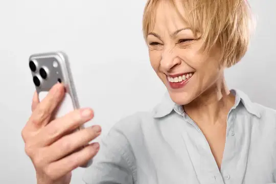 Пожилая женщина смеётся, глядя на экран смартфона