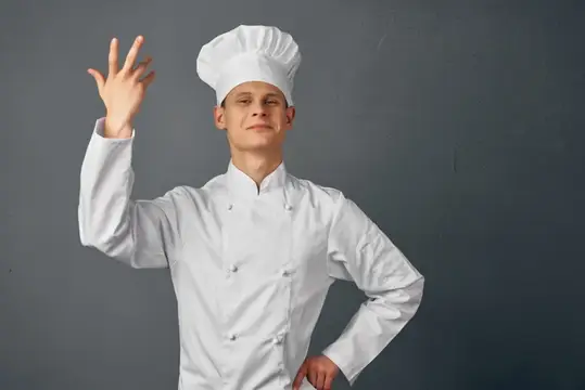 Жизнерадостный мужчина в форме шеф-повара поднимает руку в ресторане гурманов