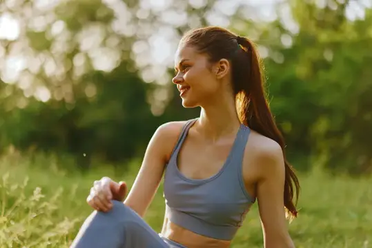 Улыбающаяся девушка в спортивной форме отдыхает на траве в парке