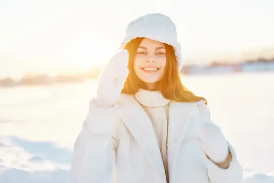 Улыбающаяся девушка в белой шапке и пальто на зимнем солнце