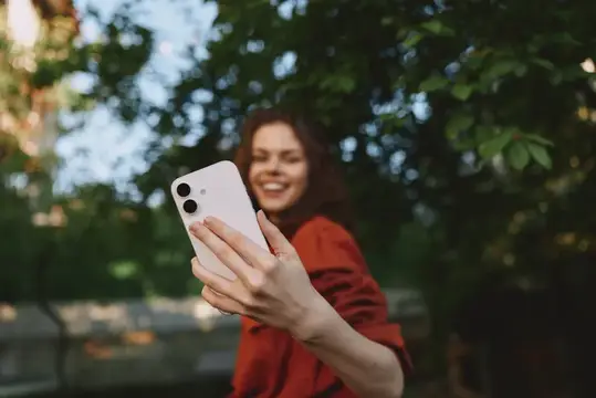 Улыбающаяся девушка в красном держит смартфон на фоне зелени