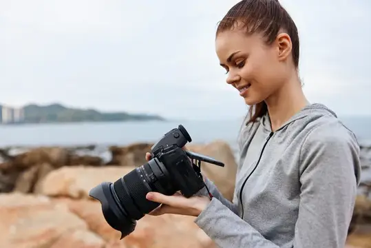 Молодая женщина рассматривает зеркальный фотоаппарат на каменистом берегу