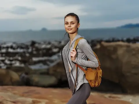 Улыбающаяся девушка с рюкзаком на скалистом берегу моря