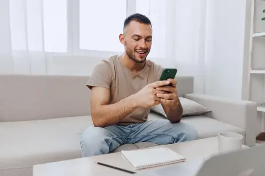 Улыбающийся мужчина с телефоном сидит на диване в светлой гостиной