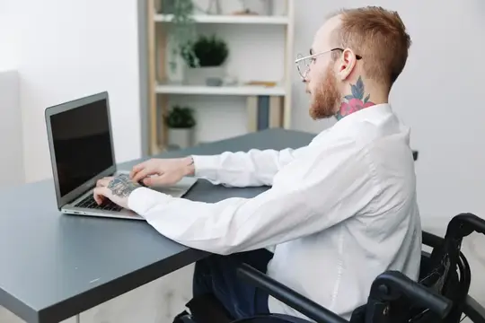 Рыжебородый мужчина в инвалидной коляске работает за ноутбуком
