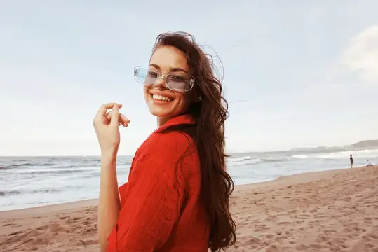 Улыбающаяся женщина в модных солнцезащитных очках, ощущающая свободу и радость на фоне красочного моря, снятого широкоугольным объективом