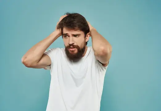 Бородатый мужчина в белой футболке хватается за голову от отчаяния