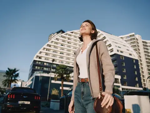 Молодая женщина с сумкой на плече на фоне белого здания