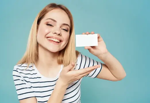 Счастливая женщина на синем фоне жестикулирует руками и держит в руке визитную карточку