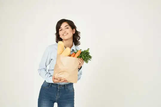 Улыбающаяся девушка с бумажным пакетом овощей и багетом