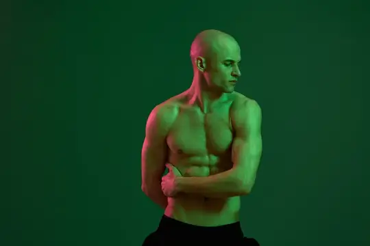 Лысый мускулистый мужчина позирует на зелёном фоне