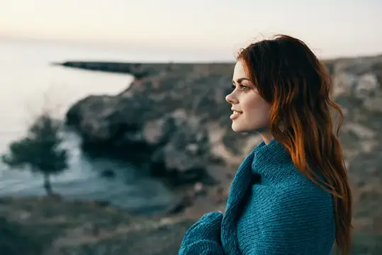 Красивая женщина в горах с пледом на плечах возле моря, модель у дерева
