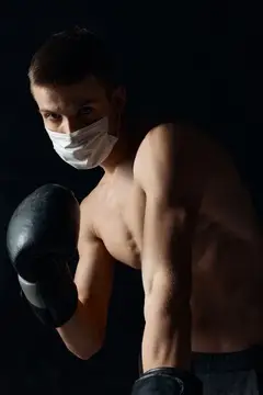 Полуобнажённый боксёр в медицинской маске на чёрном фоне