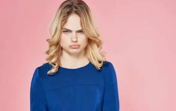 Светловолосая девушка в синем платье с недовольным лицом на розовом фоне