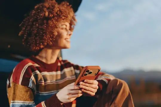 Рыжеволосая девушка со смартфоном в руках на закате