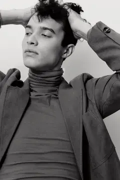 Молодой мужчина в водолазке и пиджаке поправляет волосы